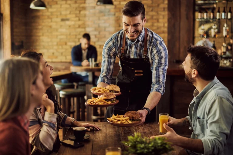 happy-waiter-serving-food-group-cheerful-friends-pub-scaled